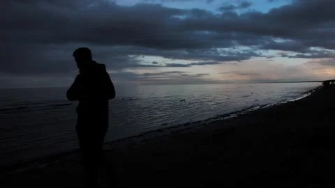 The sun sets on the beach, a persons silhouette against a cloudy sky and sea Stock Footage 279073630
