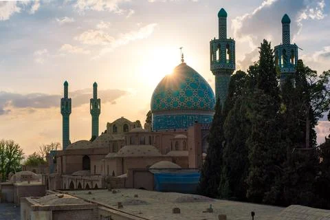 Sun sets behind the blue dome of Vali Shrine mosque viewed from a rooftop. On Stock Photos