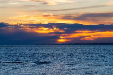 Sun sets behind dark clouds over deep blue sea. Beautiful orange sky with gol Stock Photos