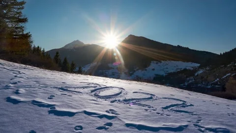 The sun sets behind the mountain, clear blue sky. Year 2022 written in the snow. 動画素材 171990341