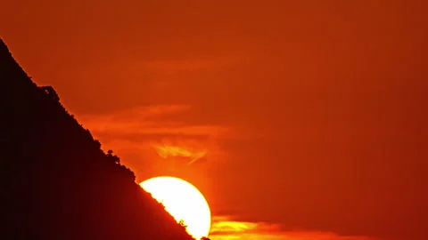 The sun sets behind a mountain with a glowing orange sky creating a dramatic Stock Footage 296418237