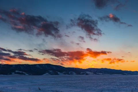 The sun sets behind the mountains and colors the clouds in winter, Altai, Rus Stock Photos