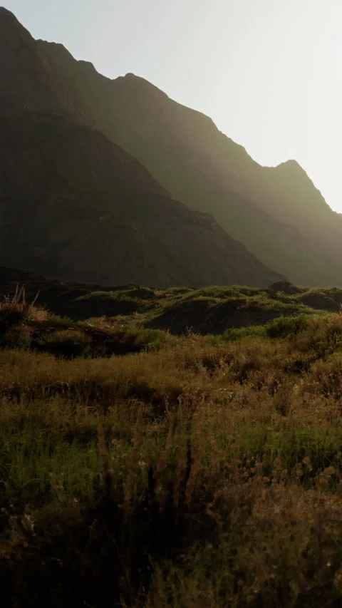 The sun sets behind mountains, casting shadows on the landscape Stock Footage 340883996