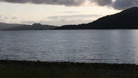 The sun sets behind a Scottish mountain, casting long shadows and sparkling Stock-Footage 80100206
