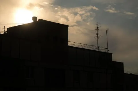 The sun sets behind a tall building and clouds. Stock Photos