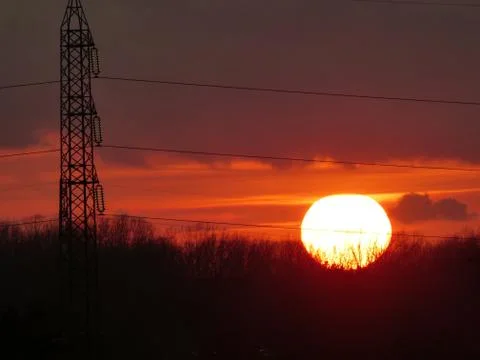 The sun sets behind trees on the horizon Stock Photos