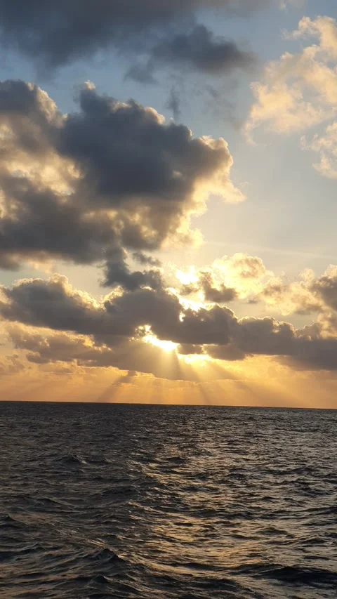 The sun sets behind wisps of clouds in the sky above the sea 動画素材 336546309