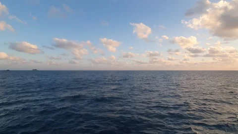 The sun sets behind wisps of clouds in the sky above the sea 動画素材 336548467