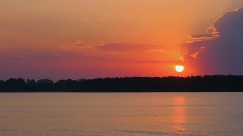 The sun sets below the horizon and is reflected in the lake. The bright orange Stock Footage 204855654