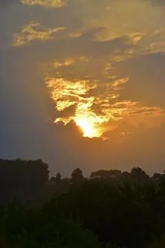 The sun sets below the horizon through light clouds. Hot summer in the Wester Stock Photos