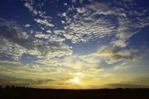 The sun sets below the horizon through light clouds. Hot summer in the Wester Stock Photos