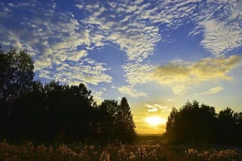 The sun sets below the horizon through light clouds. Hot summer in the Wester Stock Photos