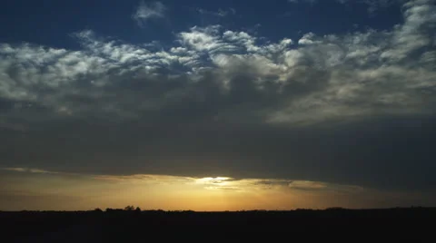 The sun sets beneath a layer of time-lapse clouds over a prairie landscape Video stock 59258409