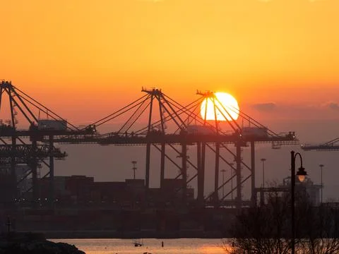 The sun sets between the large cranes of the port Stock Photos