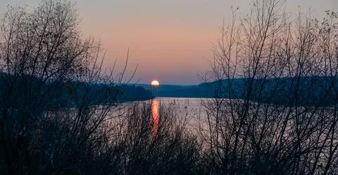 Sun sets beyond the horizon with reflections on the river surface in autumn. Stock Photos