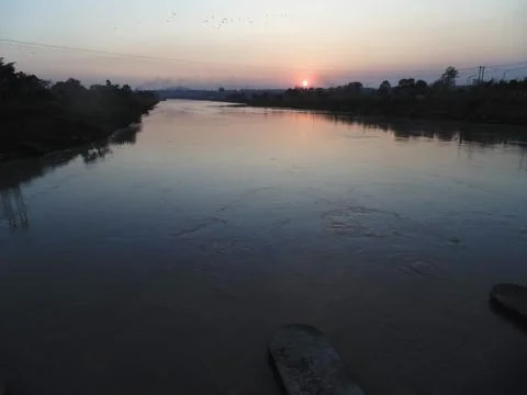 The sun sets in a blaze of color, casting a warm glow over the river Stock Photos