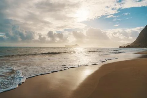 The sun sets, casting warm glow over the ocean on a cloudy day at the beach Stock Photos