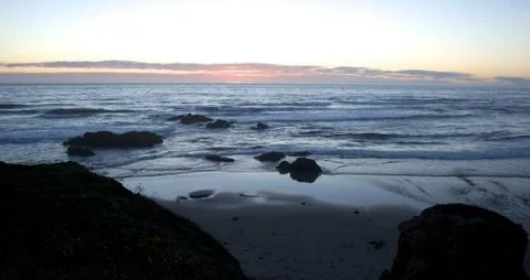 Sun sets in the distance, beach in foreground Stock Photos
