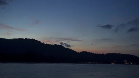 The sun sets in the evening with the sea and mountains behind and the lights Stock Footage 275592441