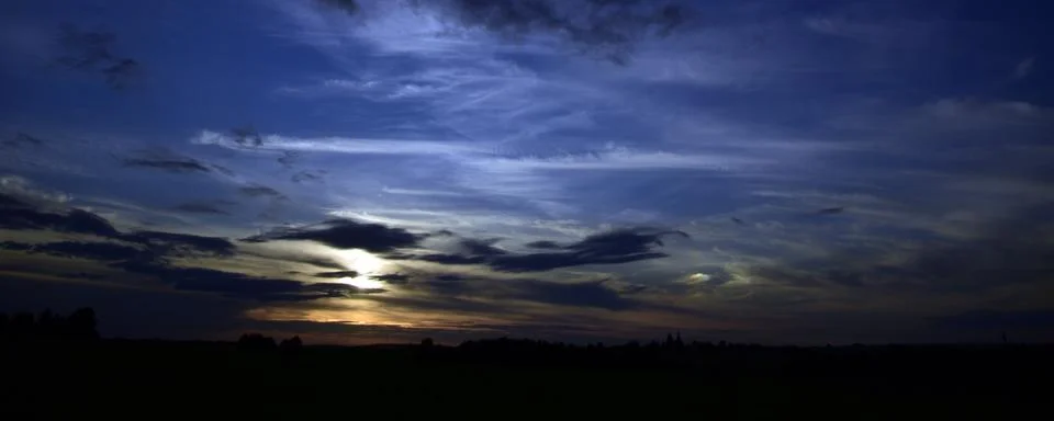 The sun sets in heavy cumulus clouds over the dark village fields. A sign of  Stock Photos