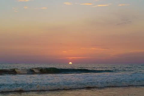 The sun sets on the horizon on a beach with waves Stock Photos