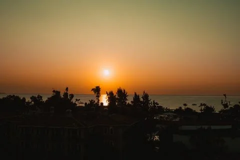 Sun sets on horizon, casting orange and yellow colors in sky. Buildings line Fotos de archivo