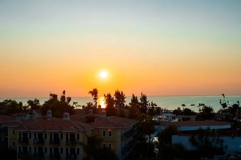Sun sets on horizon, casting orange and yellow colors in sky. Buildings line Fotos de archivo