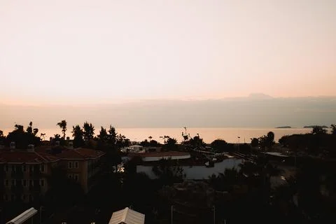 Sun sets on horizon, casting orange and yellow colors in sky. Buildings line Fotos de archivo