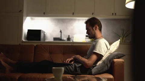 As the sun sets, a man finds solace on his cozy couch in a serene atmosphere Stock Footage 289963984