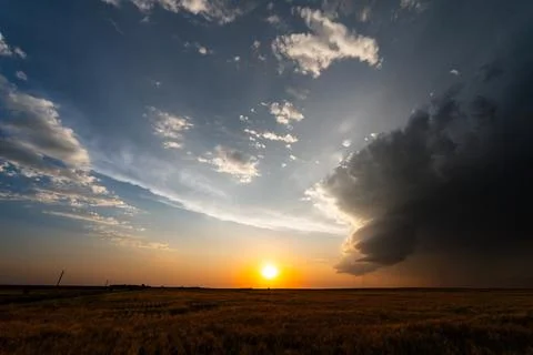 The sun sets over beautiful fields as dark storm clouds drift away, creating  Stock Photos