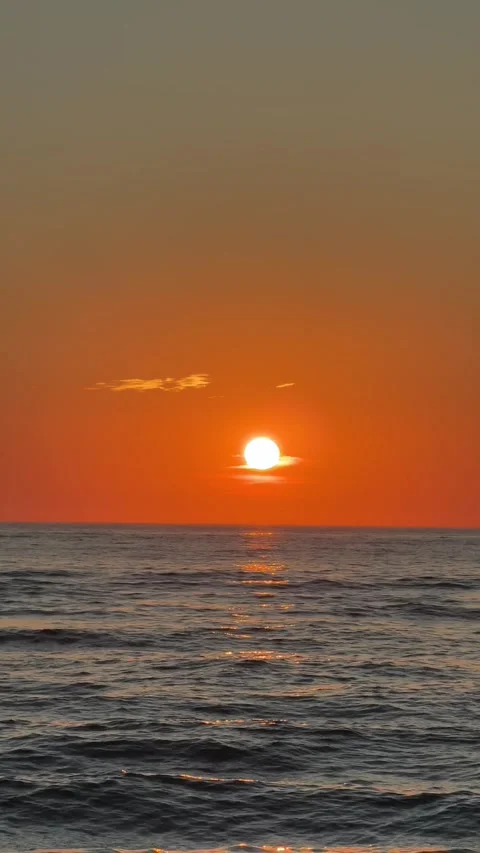 The Sun Sets Over the Calm Ocean, Casting a Warm Orange Glow Across the Gentle Stock Footage 334643261