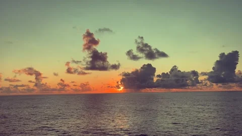 Sun sets over calm ocean with dramatic clouds and warm colors Stock Footage 338282060
