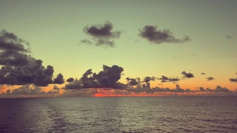 The sun sets over a calm ocean horizon with scattered clouds in a warm sky 動画素材 338282805