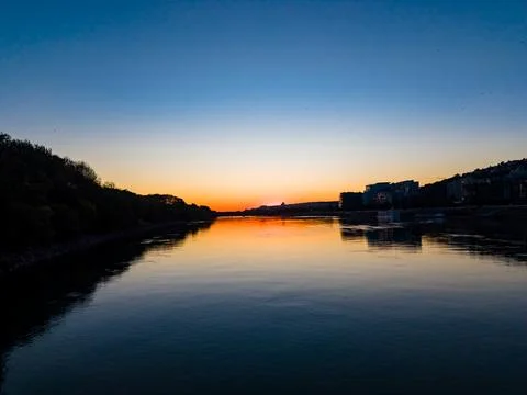 The sun sets over a calm river reflecting colors of orange and blue. Building Stock Photos