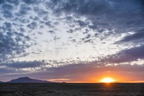The sun sets over a desert landscape with mountains behind it Stock Photos