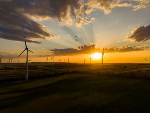 Sun sets over fields with wind turbines spinning gently in the breeze. The sk Stock Photos