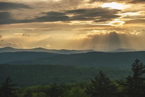 The sun sets over the forest and mountains, light pours through the clouds. Stock Photos