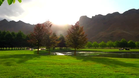 The sun sets over high mountains and illuminates the lake and the green lawn Stock Footage 131773975