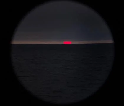 The sun sets over the horizon through clouds photographed through binoculars Stock Photos