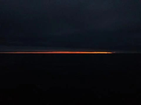 The sun sets over the horizon through clouds Stock Photos