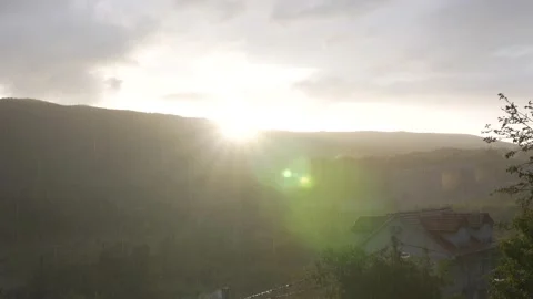 The sun sets over the mountain and it rains blindly over the eco village Stock Footage 134538437
