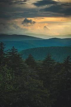 The sun sets over the mountains in the forest, with the clouds in the sky. Stock Photos