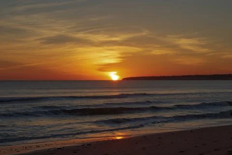 Sun sets over the ocean at Albufeira  while waves roll in along the shore at a Fotos Stock