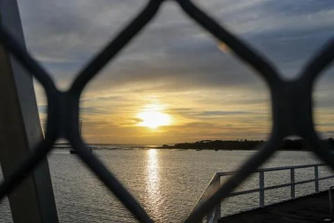 The sun sets over the ocean, framed through a fence Stock Photos