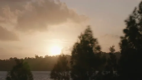 Sun sets over river behind dark trees. Golden clouds, sunbeams shine through Stock-Footage 203999413