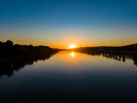 Sun sets over the river, casting warm light on the water. The sky changes col Stock Photos