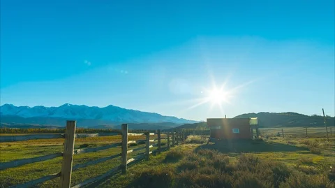 The sun sets over the snow-capped mountain peaks. Wooden house and hedge in the Video stock 102499984