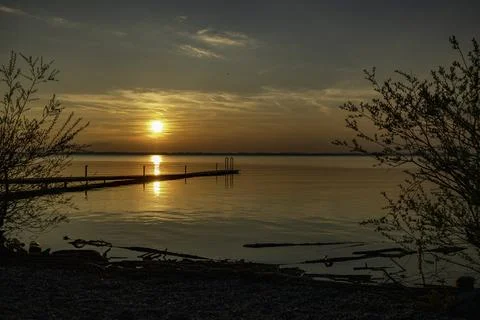 The sun sets over the water with trees in the foreground a wooden decking o.. Stock Photos