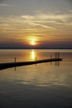 The sun sets over the water with trees in the foreground a wooden decking o.. Stock Photos