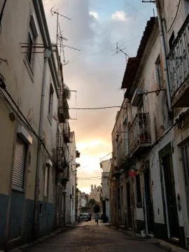 The sun sets through a narrow old town street with high buildings on each side Stock Photos